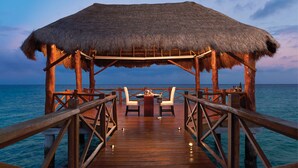 A wooden deck with a thatched roof structure, two white chairs, a small table, and a bottle of wine. - The Fives Beach Hotel - Á la Carte All Inclusive (Playa del Carmen)