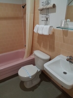 A bathroom with a pink bathtub, a white toilet, and a white sink. - Rodeway Inn La Grande - Island City (La Grande)
