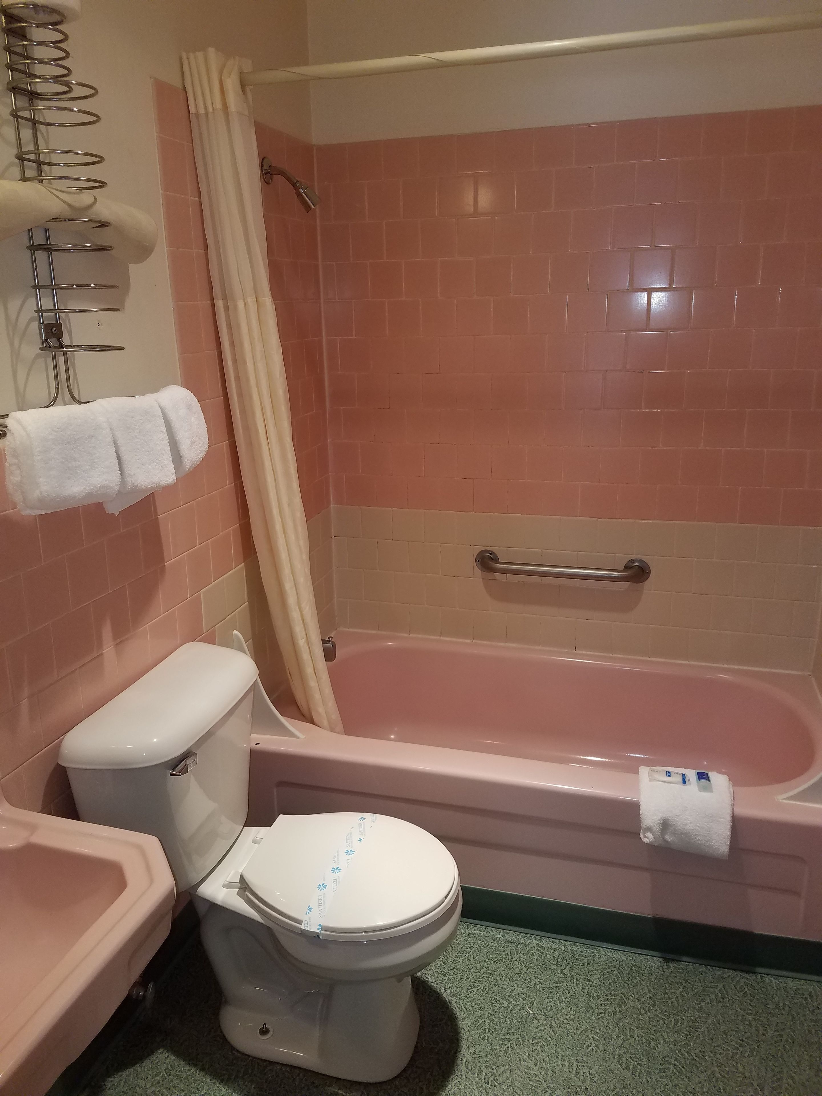 Un bany amb una banyera rosa, un vàter blanc i una cortina de dutxa.