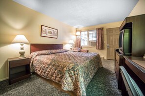 A hotel room with a bed, two bedside lamps, a television, and a window with curtains. - Rodeway Inn La Grande - Island City (La Grande)