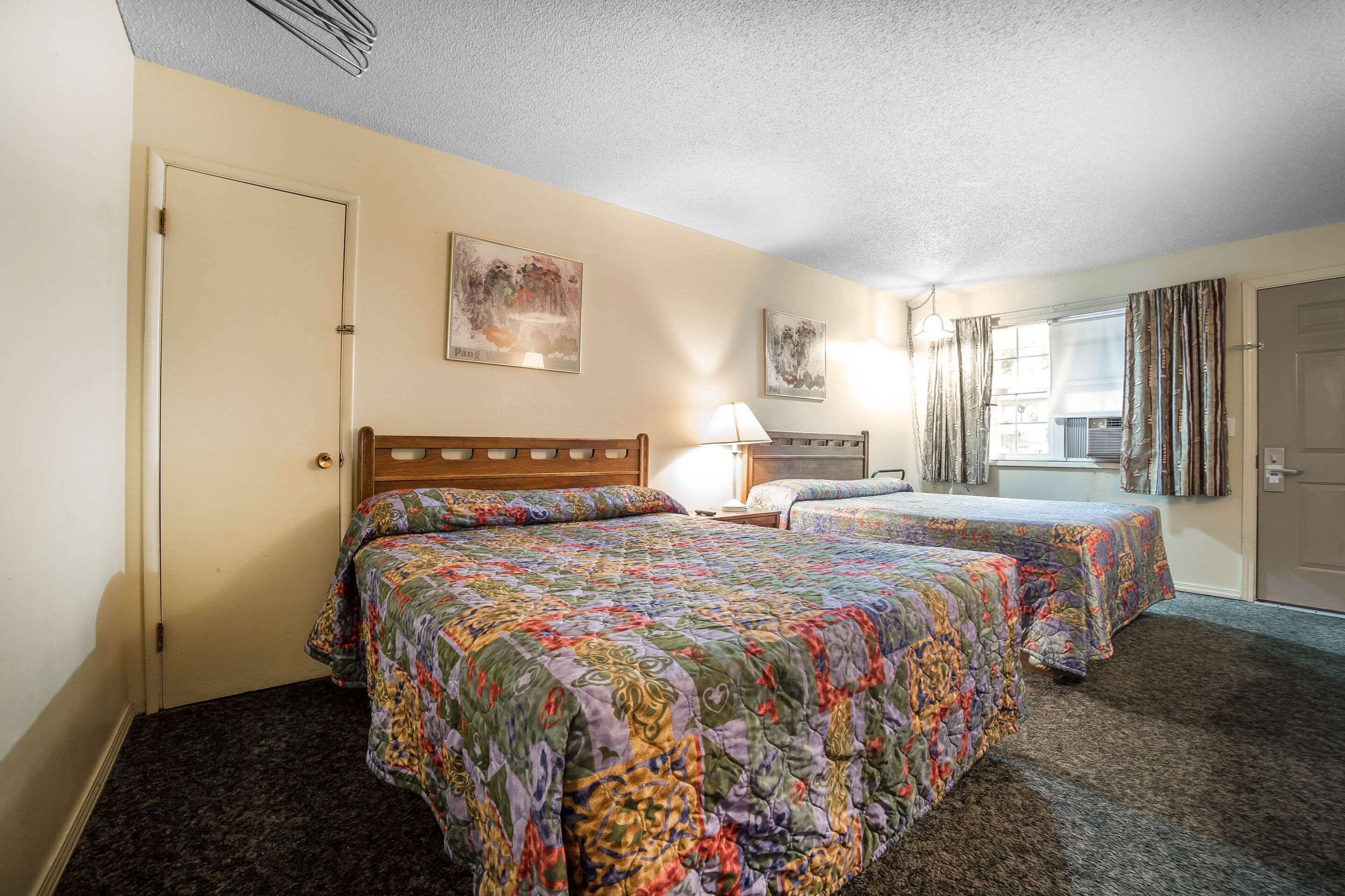 A hotel room with two beds, a window with curtains, a lamp, and artwork on the walls.
