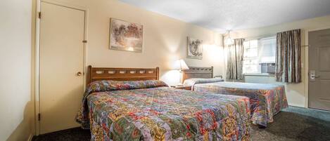 A hotel room with two beds, a window with curtains, a lamp, and artwork on the walls.