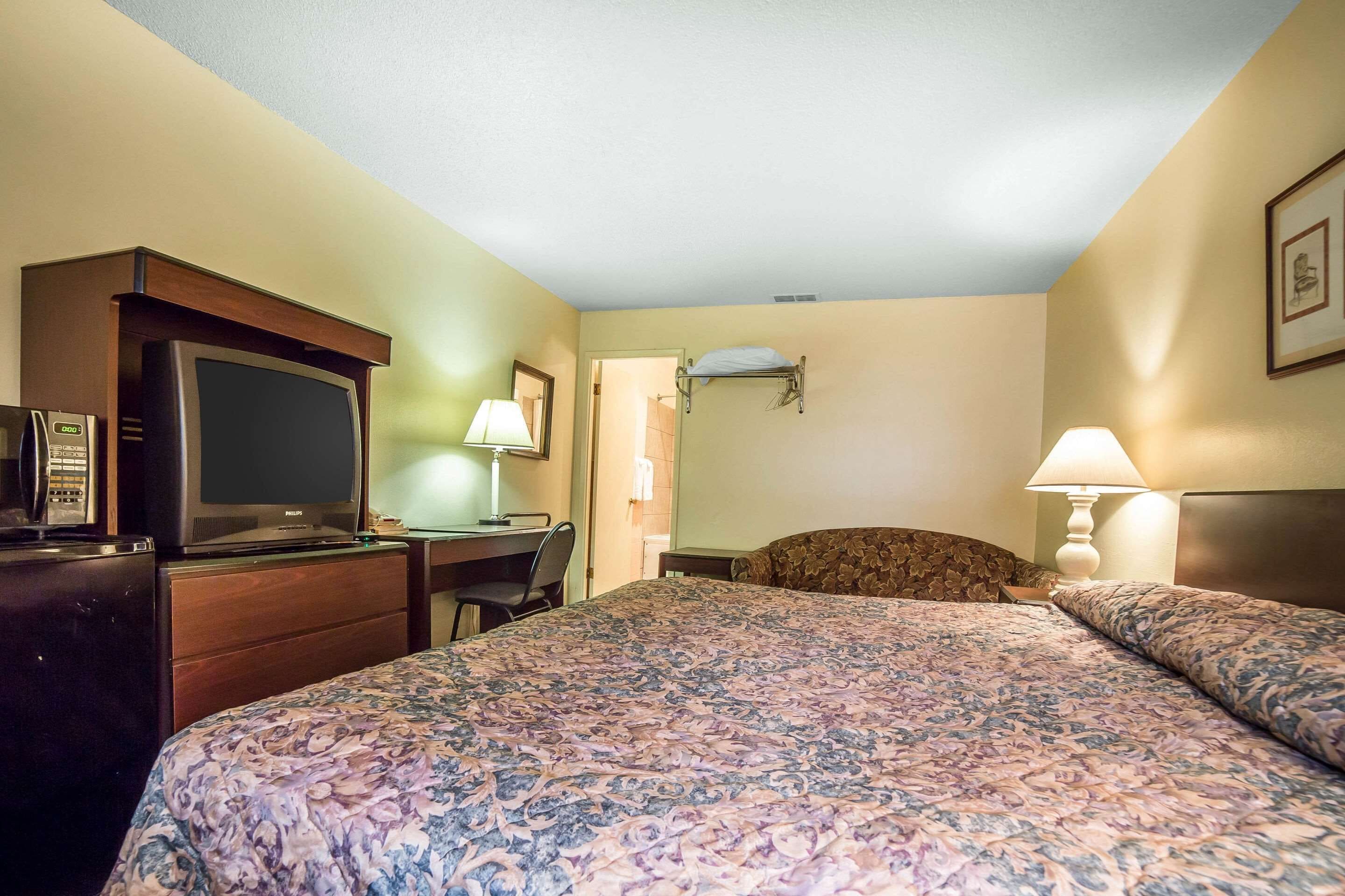 A hotel room with a bed, a desk, a television, and a lamp.