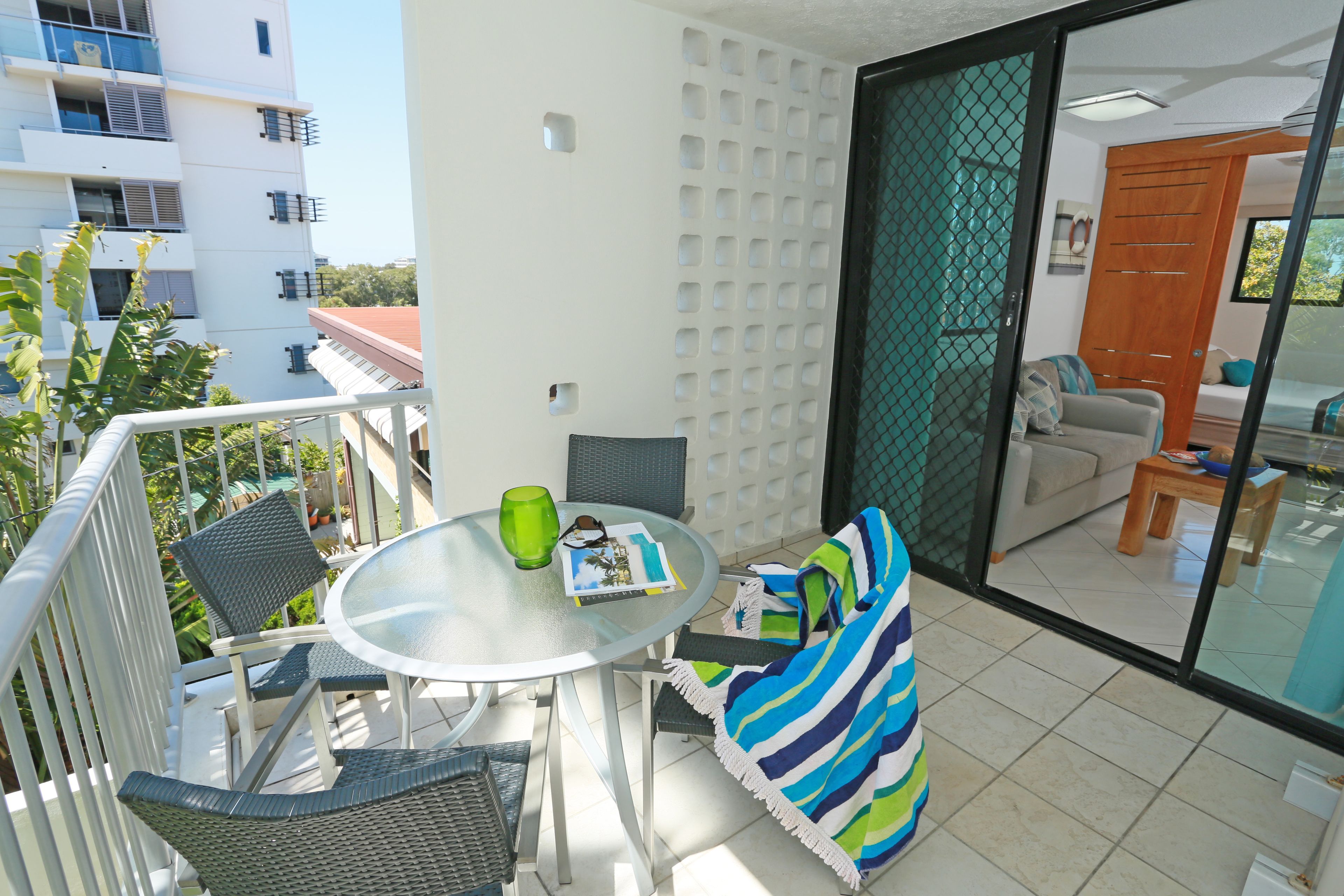 Un balcon avec une table en verre, des chaises et une serviette à rayures.