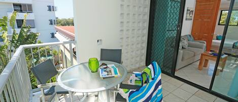 Un balcon avec une table en verre, des chaises et une serviette à rayures.