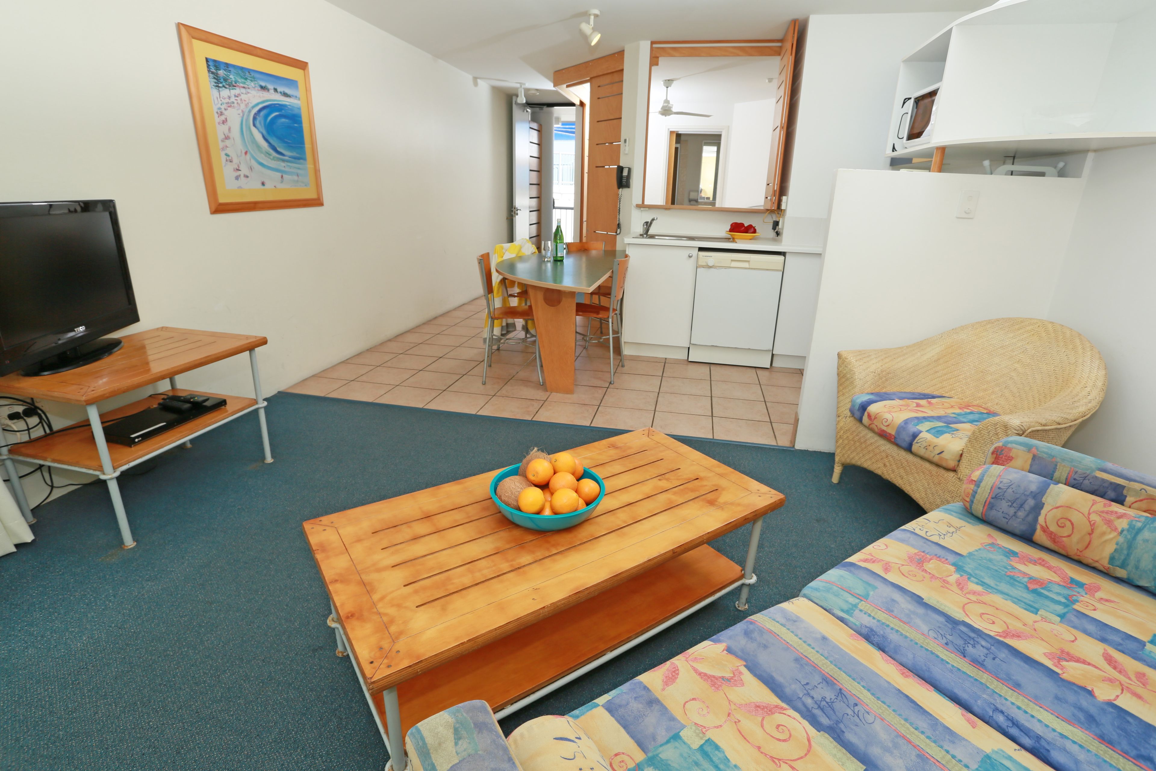 A compact living space with a wooden table, a sofa, a television, a kitchen area, and a dining table.