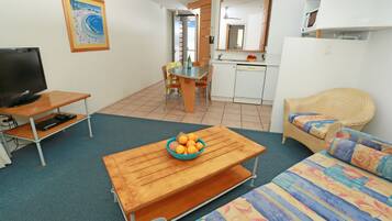 A compact living space with a wooden table, a sofa, a television, a kitchen area, and a dining table.