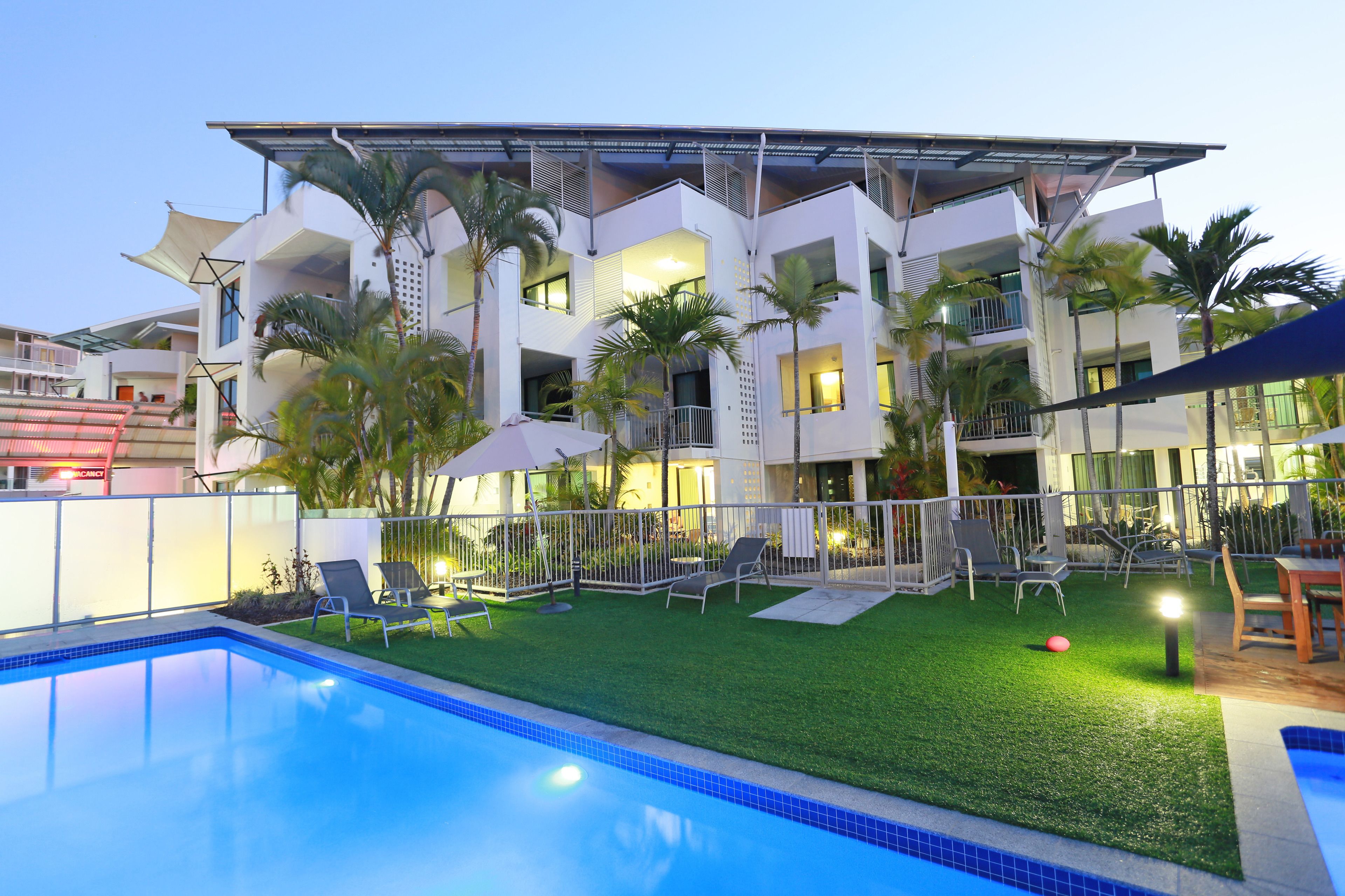 A modern hotel with a swimming pool, outdoor seating, and palm trees.