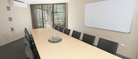 A conference room with a long table, chairs, a whiteboard, and a window with blinds.