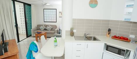 A modern kitchen with white cabinets, a dining table, and a small island. There is a clock on the wall and a window with a view of the outside.