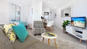 Et moderne, lyst værelse med seng, sofa, spiseplads og fjernsyn.