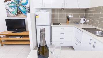 A modern kitchen with white cabinets, a built-in oven, a sink, and a countertop with a bottle and glasses.