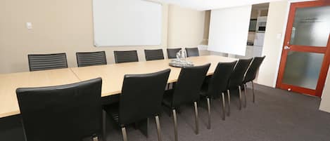 A conference room with a long table, black chairs, a whiteboard, and a door with a frosted glass panel.