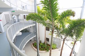 A multi-level indoor atrium with a central garden area, featuring a palm tree and various plants.