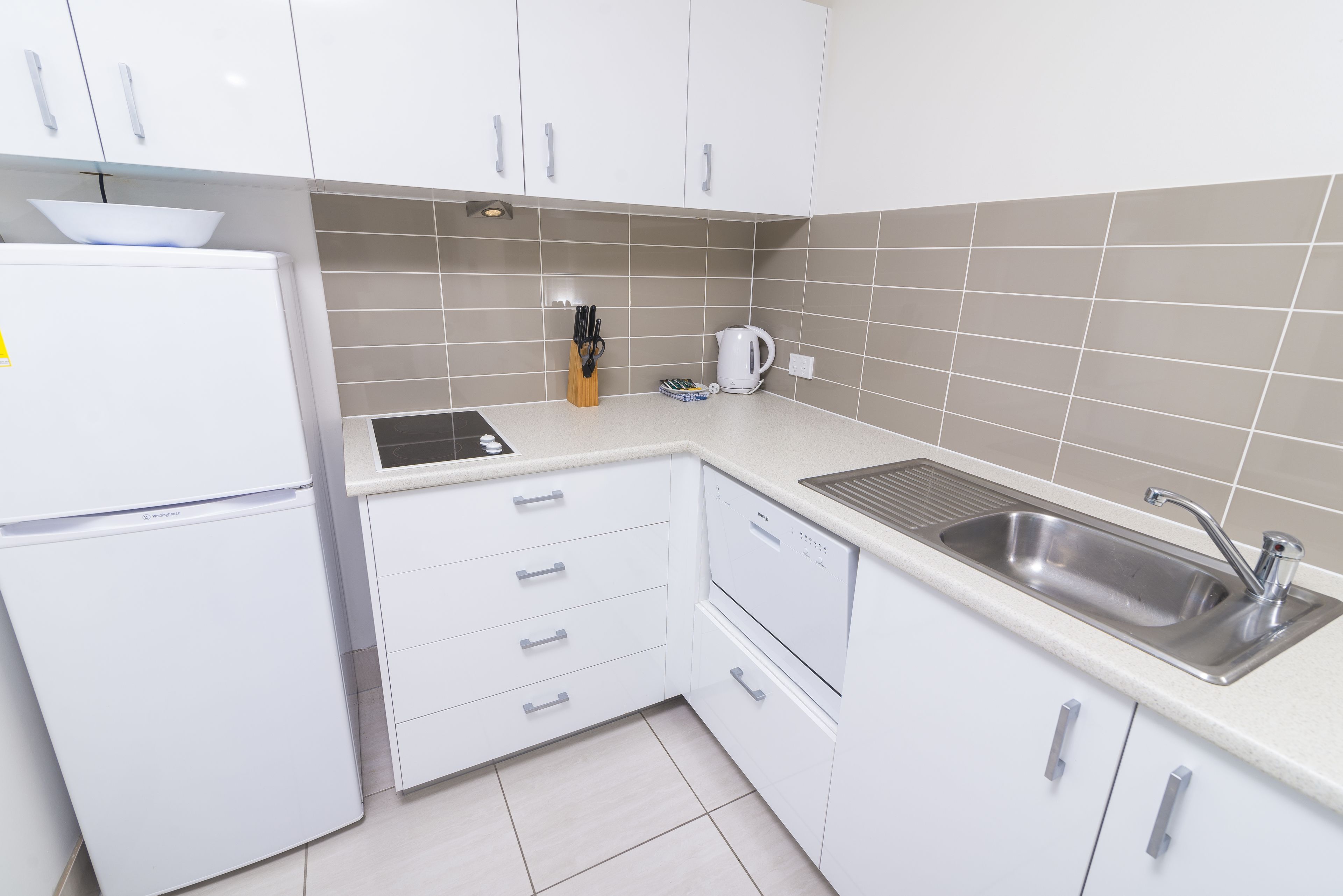 A modern kitchen with white cabinets, a built-in dishwasher, and a stainless steel sink.