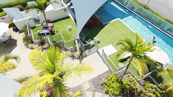 A rooftop pool area with a clear view of the pool, surrounded by palm trees and a well-maintained lawn.