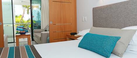A hotel room with a bed, a nightstand, a wooden wardrobe, and a view of the outside balcony.