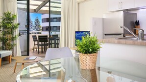 Et moderne køkken med et indbygget køleskab, en vask og et vindue med udsigt til en balkon. Der er et spiseområde med et bord og stole, og en potteplante på disken.