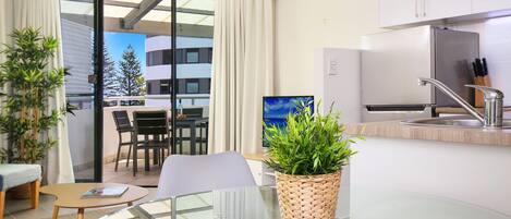 Una cocina moderna con refrigerador empotrado, un lavamanos y una ventana con vista a un balcón. Hay un comedor con mesa y sillas, y una planta en maceta sobre la encimera.