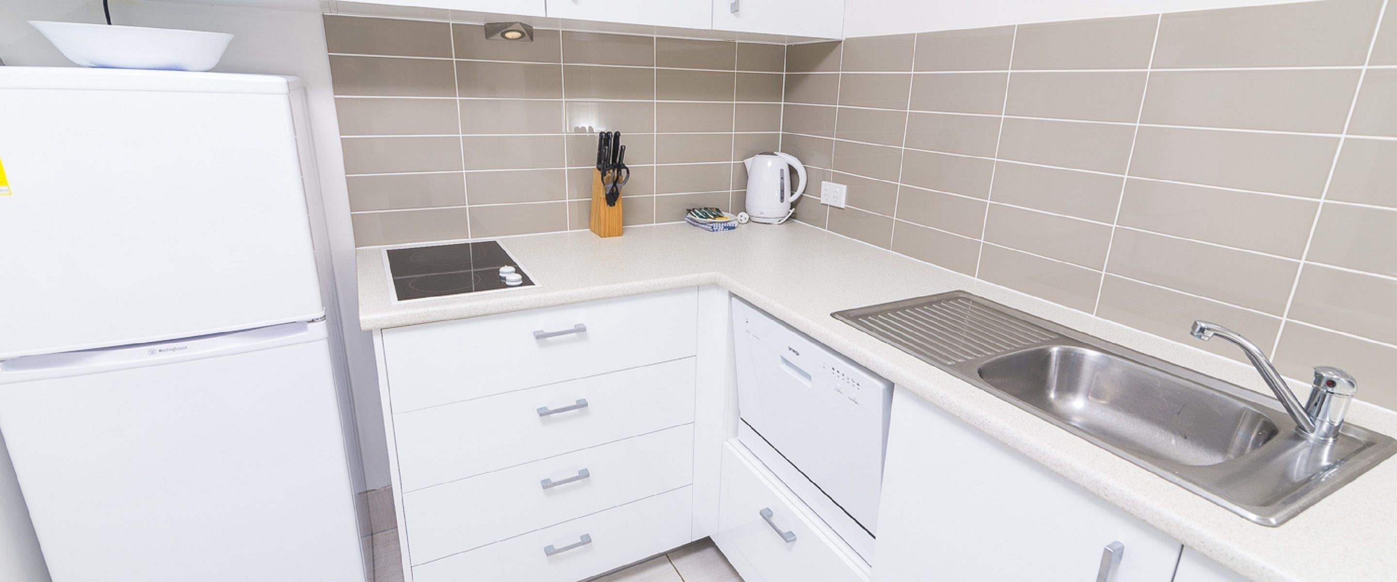 A modern kitchen with a built-in dishwasher, a stainless steel sink, and a kettle.