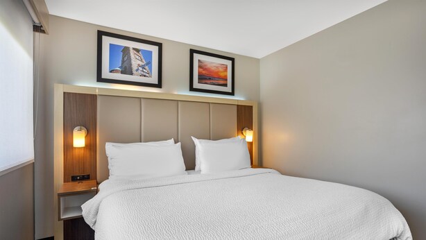 A hotel room with a large bed, two bedside tables, a headboard with built-in lighting, and two framed pictures on the wall.