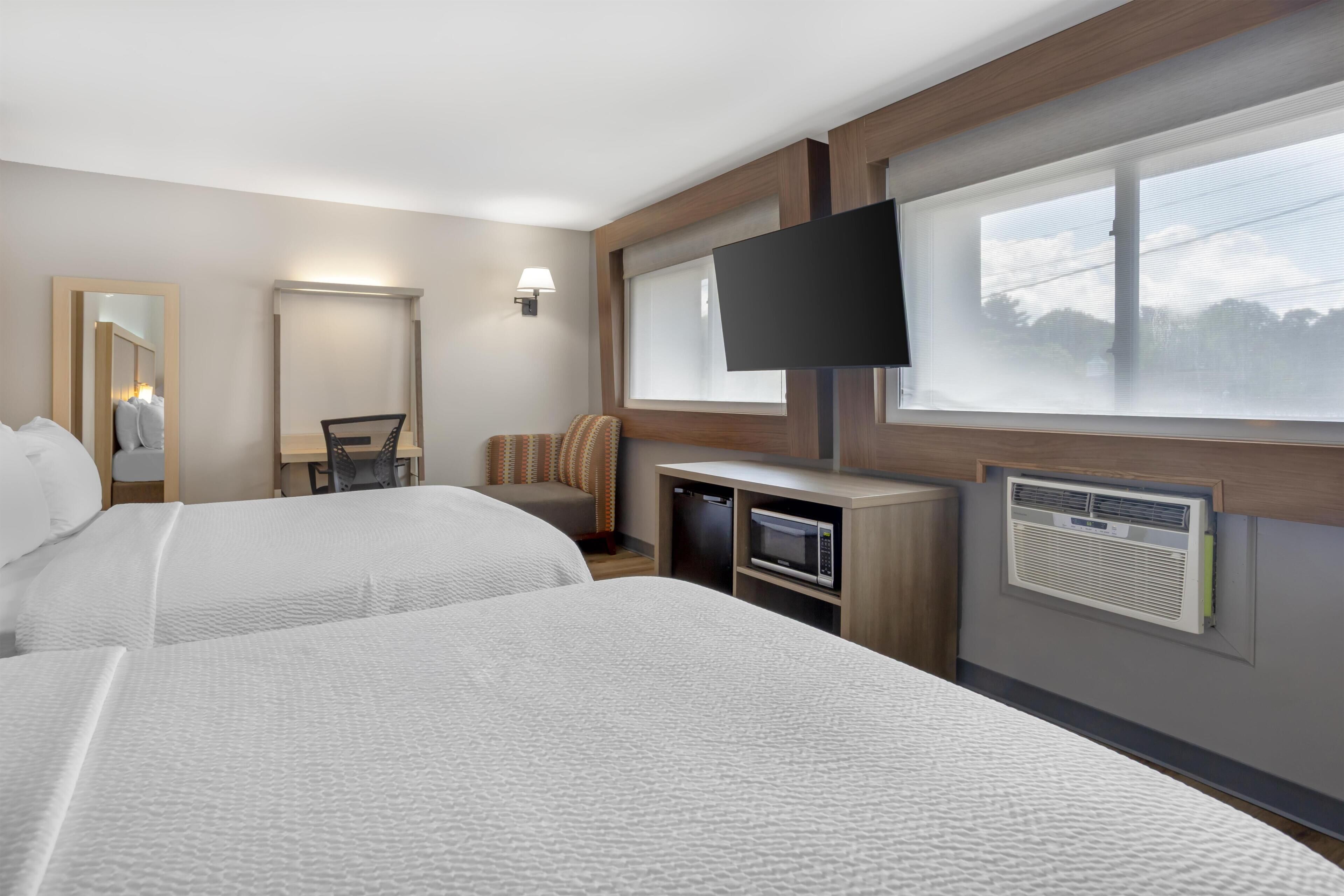 A hotel room with two beds, a desk, a chair, a flat-screen TV, and a window with blinds.