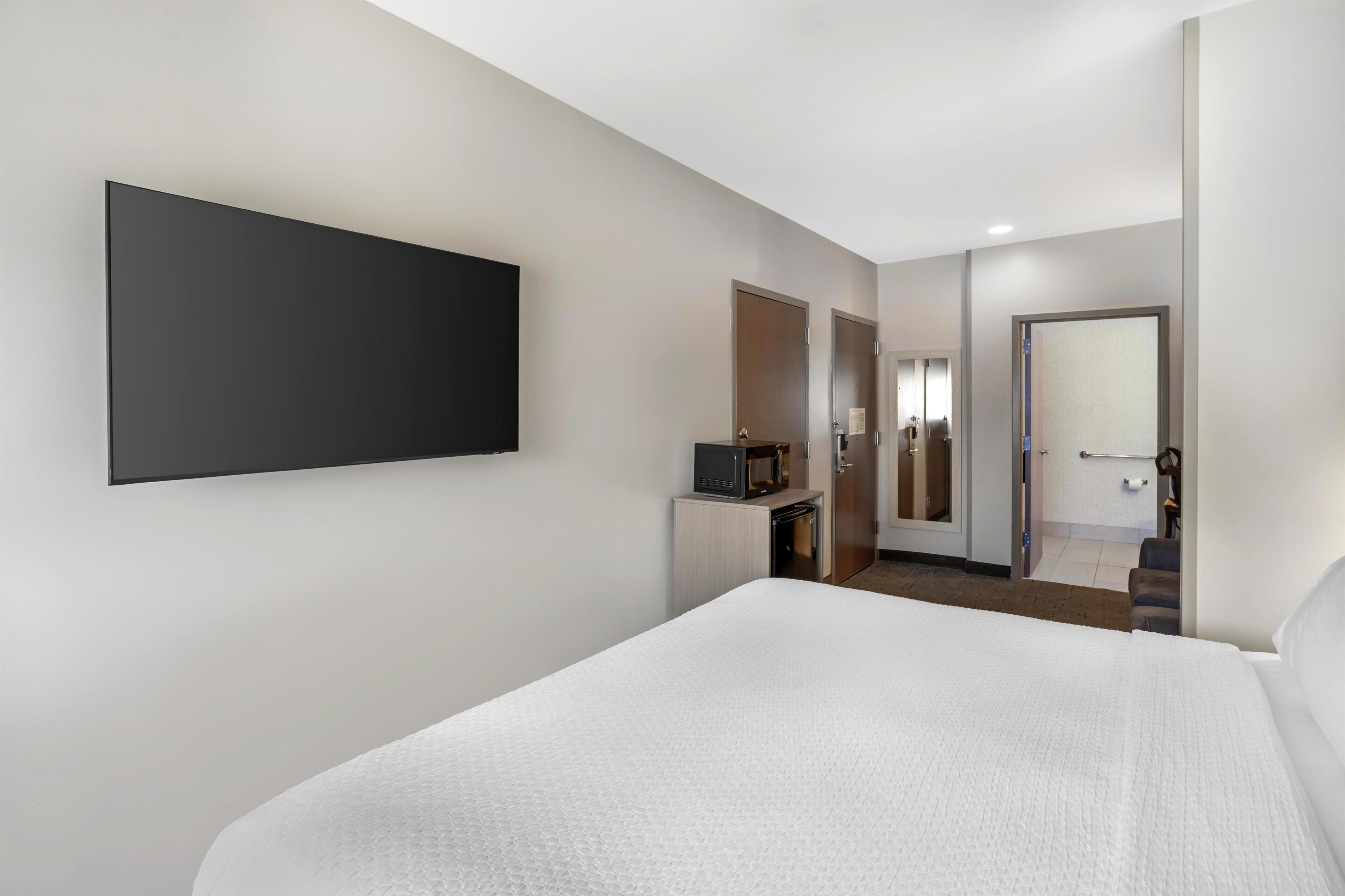 Une chambre d’hôtel dotée d’un grand lit, d’un téléviseur à écran plat fixé au mur, d’une petite kitchenette et d’une salle de bain avec un miroir et des toilettes.