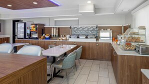 A modern cafe with a self-service station, seating area, and a display case with pastries.