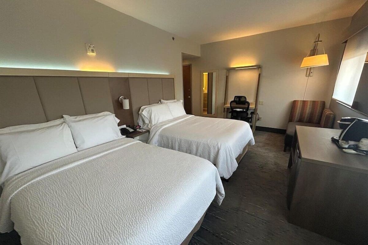 Une chambre d’hôtel avec deux lits, un bureau, une chaise et un téléviseur.