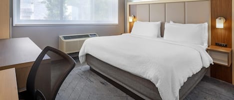 A hotel room with a bed, a desk, a chair, a window, and two wall-mounted lamps.