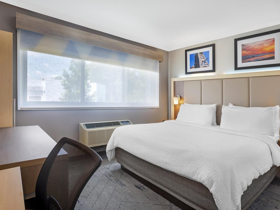 A hotel room with a bed, a desk, a chair, a window, and two wall-mounted lamps.