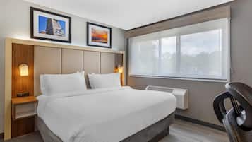 Een hotelkamer met een bed, nachtkastje, bureau, stoel, raam en twee ingelijste foto's aan de muur.