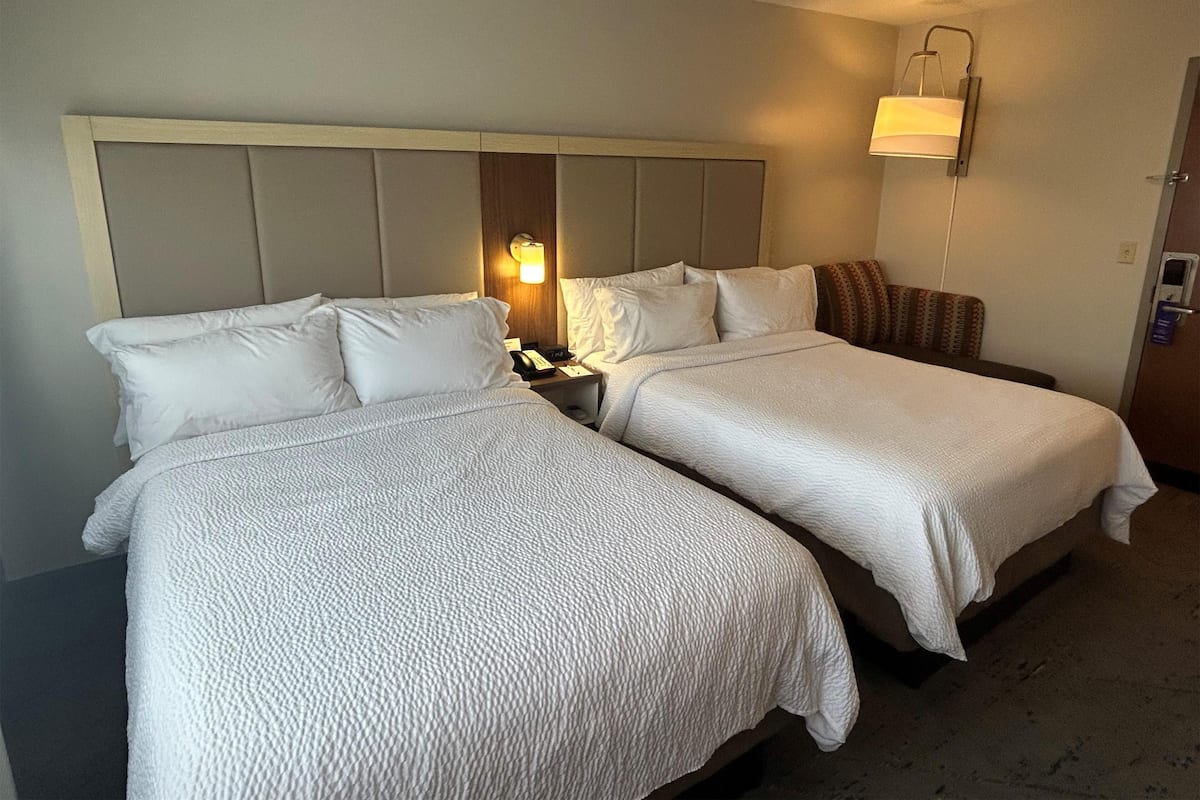Une chambre d’hôtel avec deux lits, une tête de lit, des lampes de chevet et un luminaire fixé au mur.