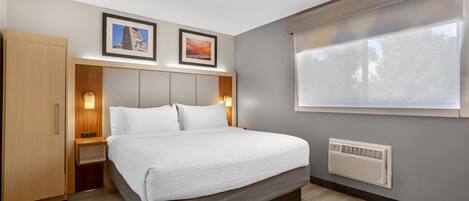 A modern hotel room with a bed, bedside tables, a wardrobe, a window with blinds, and two framed pictures on the wall.
