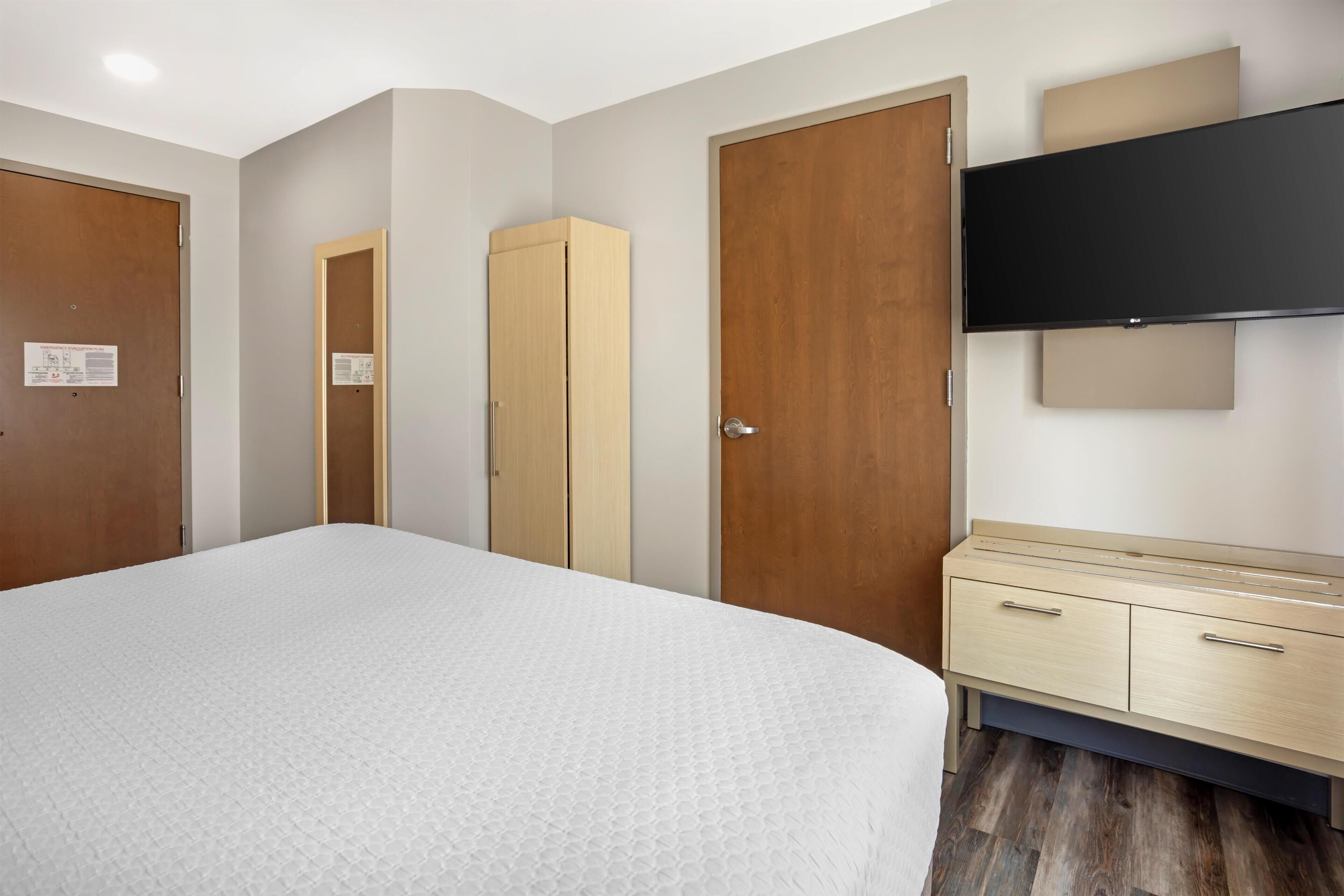 A hotel room with a bed, wardrobe, and a TV mounted on the wall.
