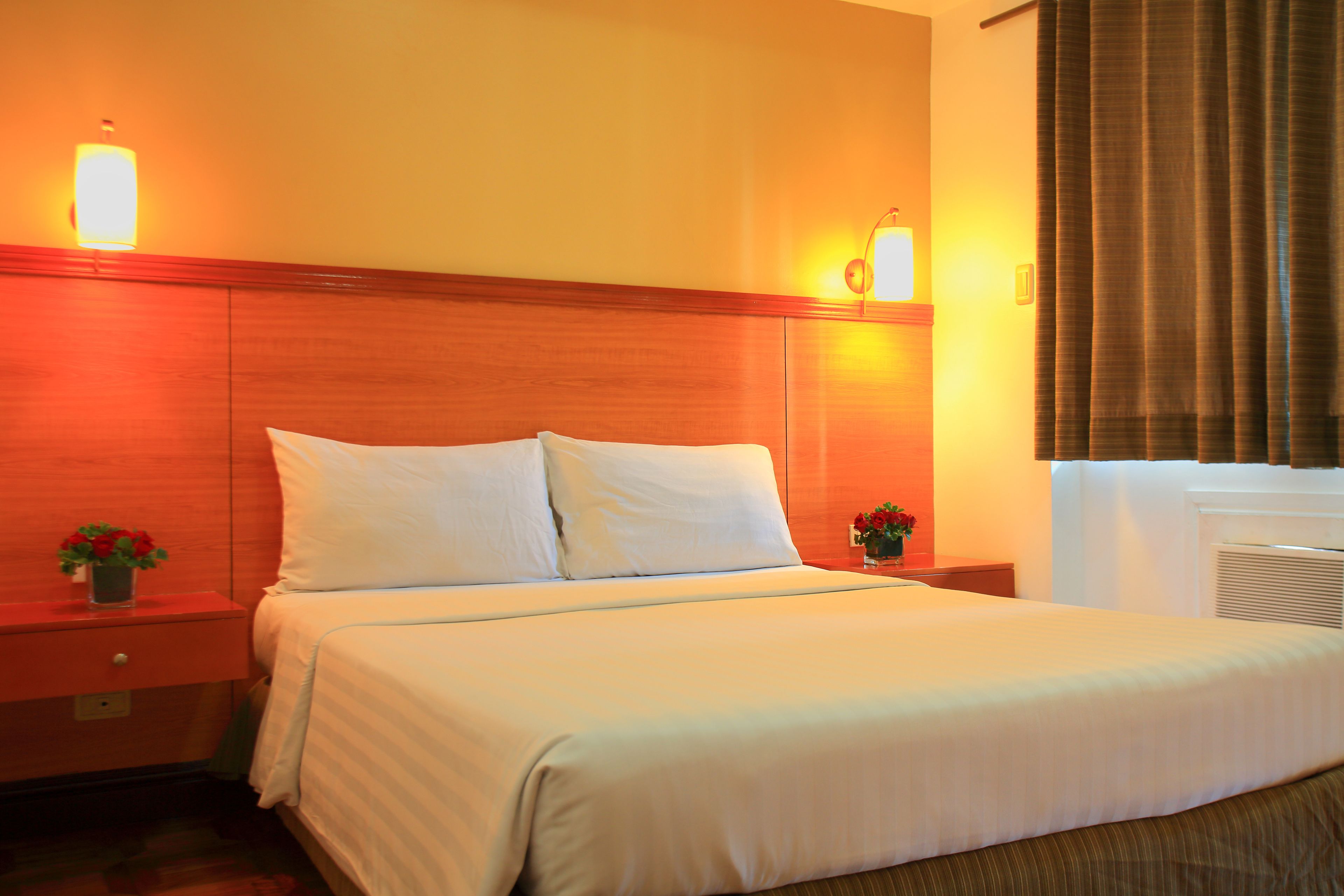 A hotel room with a large bed, two bedside tables, and a nightstand with a vase of flowers.