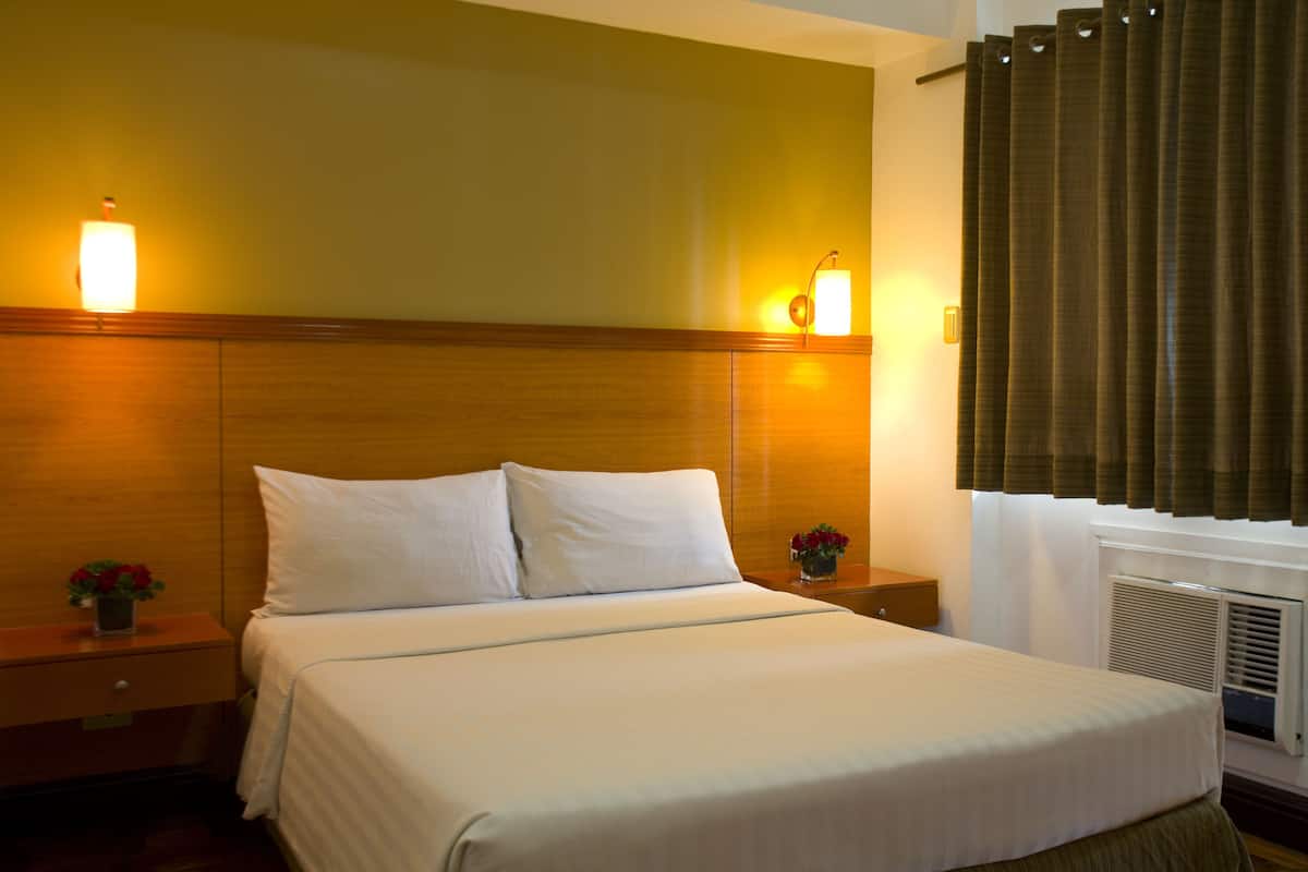 A hotel room with a bed, nightstands, a lamp, and a window with curtains.