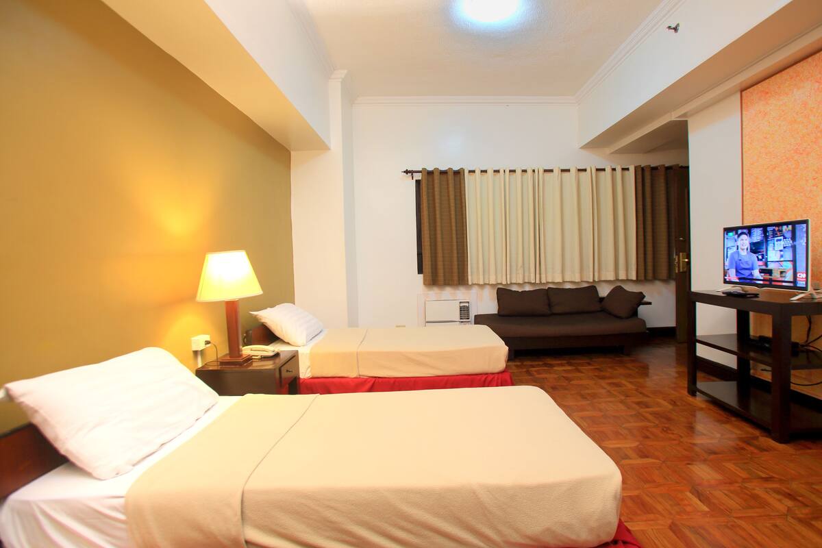 A hotel room with two beds, a sofa, a TV, and a desk.