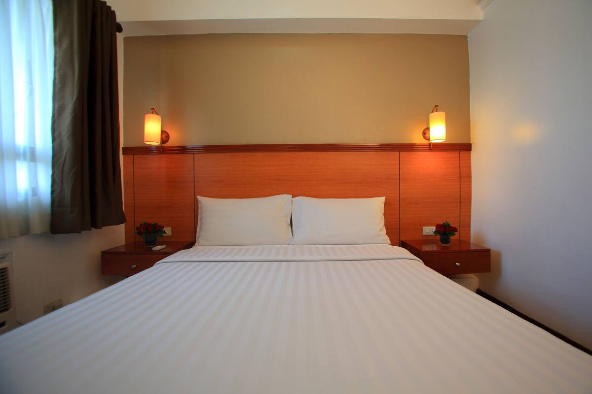 A hotel room with a large bed, two bedside tables with lamps, and a window with curtains.