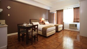 A hotel room with two beds, a dining table with chairs, a lamp, and a window with curtains. - BSA Suites Makati (Makati)