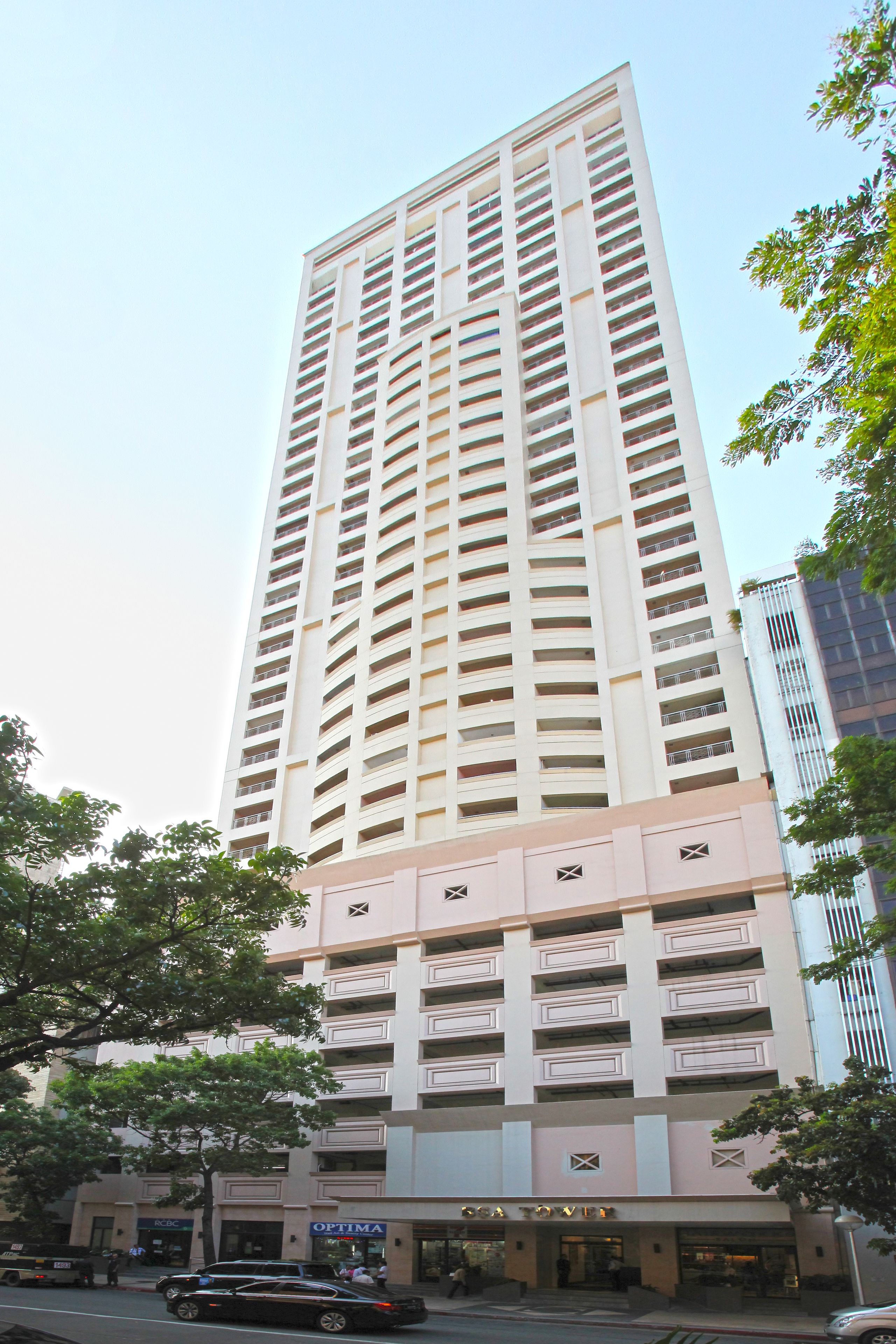 A tall, multi-story building with a modern architectural design, featuring a series of balconies and a ground-level commercial space with visible signage.