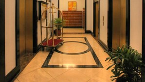 A hotel corridor with two elevators, a central light fixture, and a potted plant. - BSA Tower Serviced Residences (Makati)