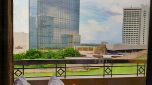 A hotel room with a view of a cityscape through large windows, featuring modern buildings and a green park. - BSA Tower Serviced Residences (Makati)