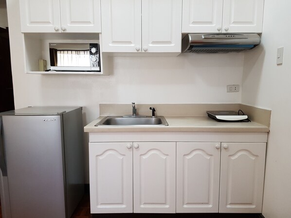Una cocina con armarios blancos, un lavamanos, un microondas y un horno empotrado.
