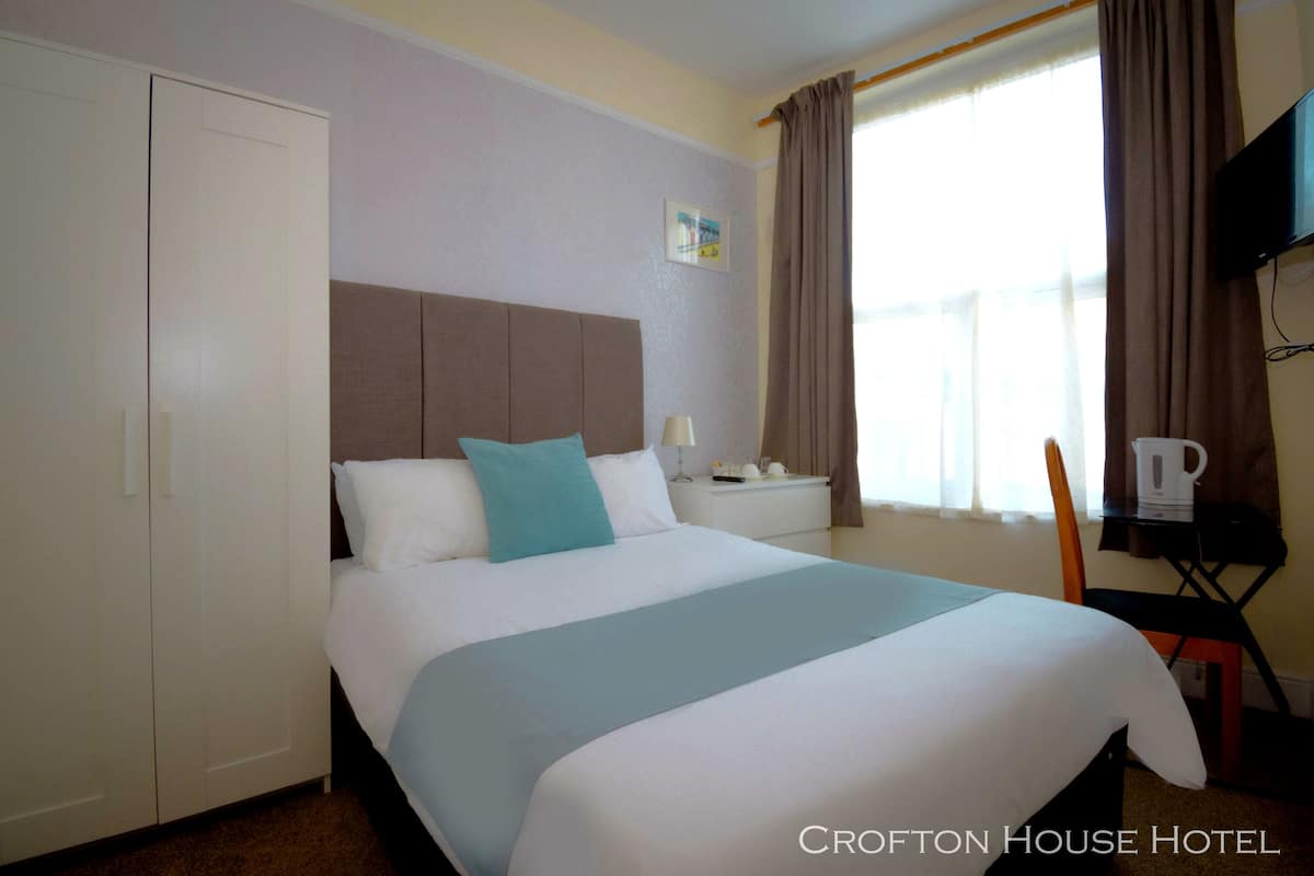 A hotel room with a bed, a nightstand, a chair, a wardrobe, and a television on the wall.