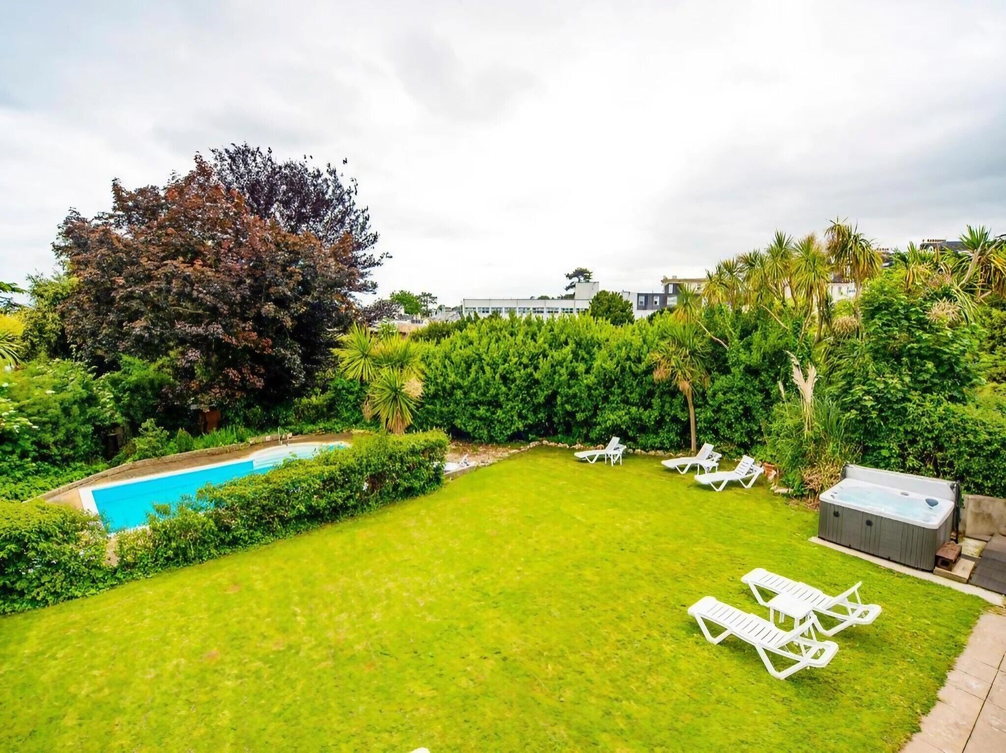 A backyard with a swimming pool, green lawn, and white lounge chairs.