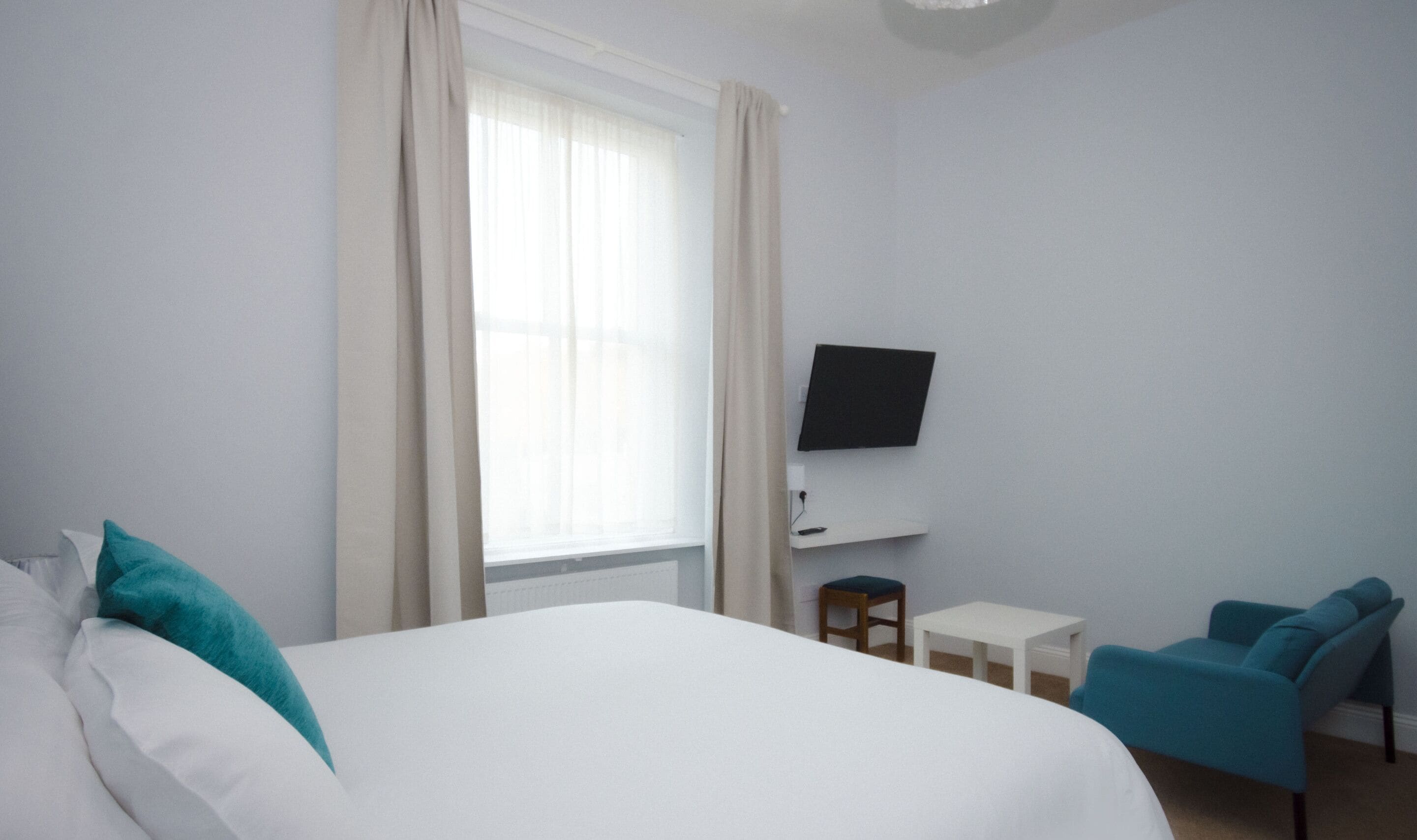 A hotel room with a bed, a TV mounted on the wall, a small table, and two chairs.