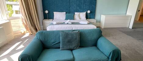 A bedroom with a bed, a sofa, a dresser, and a chandelier.