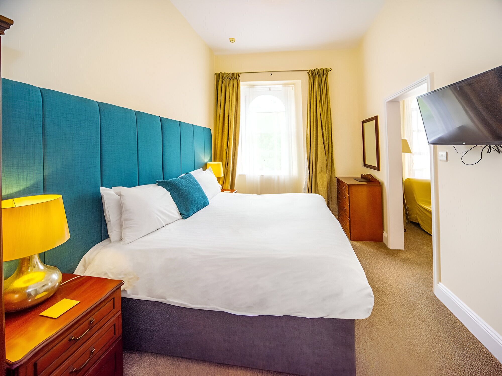 Ein Hotelzimmer mit einem großen Bett, einem Nachttisch aus Holz, einem Fernseher und einem Fenster mit Vorhängen.