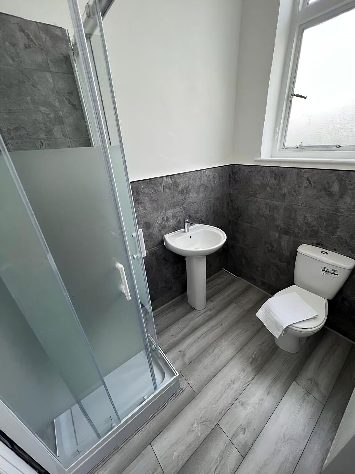 A bathroom with a glass shower enclosure, a pedestal sink, and a toilet.